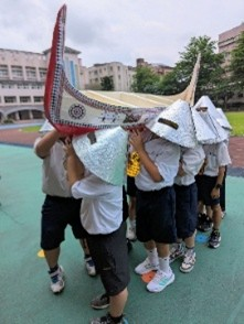 圖為雅美族大船下水祭與髮舞，視覺重點： 黃金飾片、銀盔、拼板舟模型身繪有紅白黑的「船眼睛」紋樣。