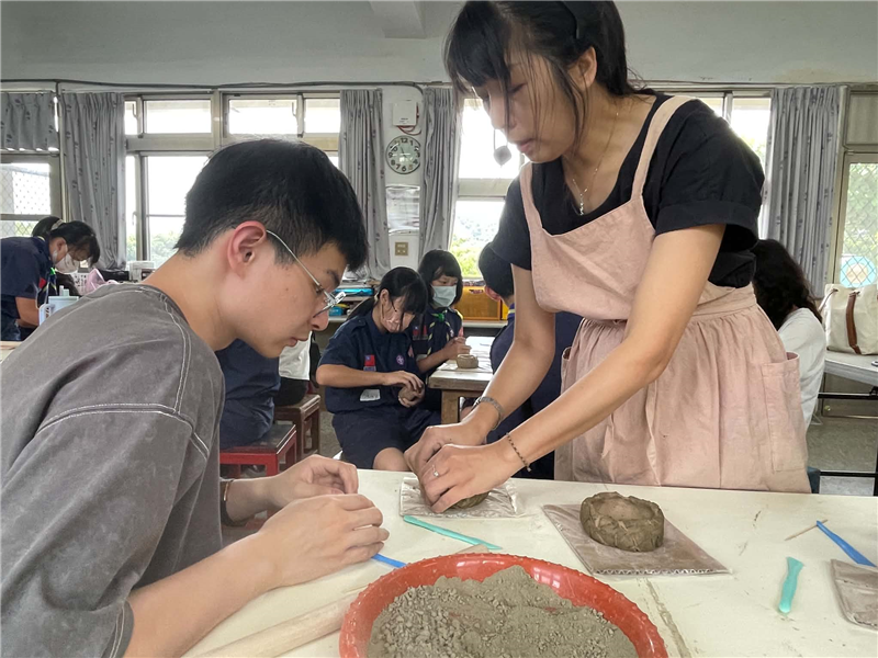 王老師指導學生如何將陶土捏成花器